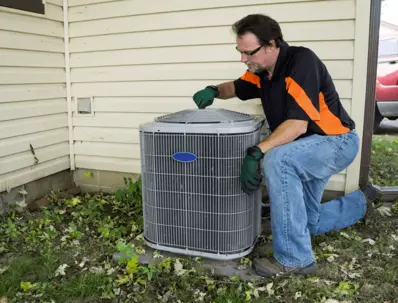 An HVAC technician kneels beside an air conditioner.